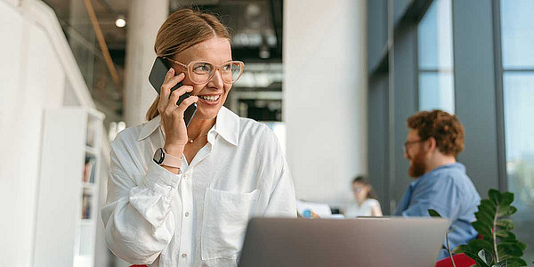 Eine telefonierende Frau sitzt vor einem Laptop